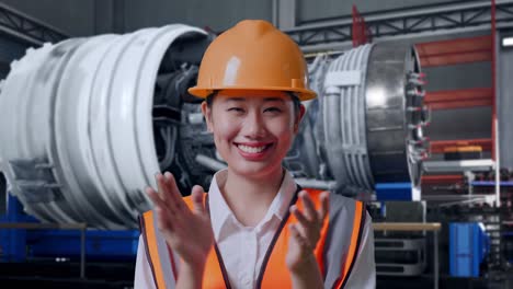 Close Up Of Asian Female Engineer With Safety Helmet Smiling And Clapping Her Hands While Standing With Airplane Engine Maintenance Conducted