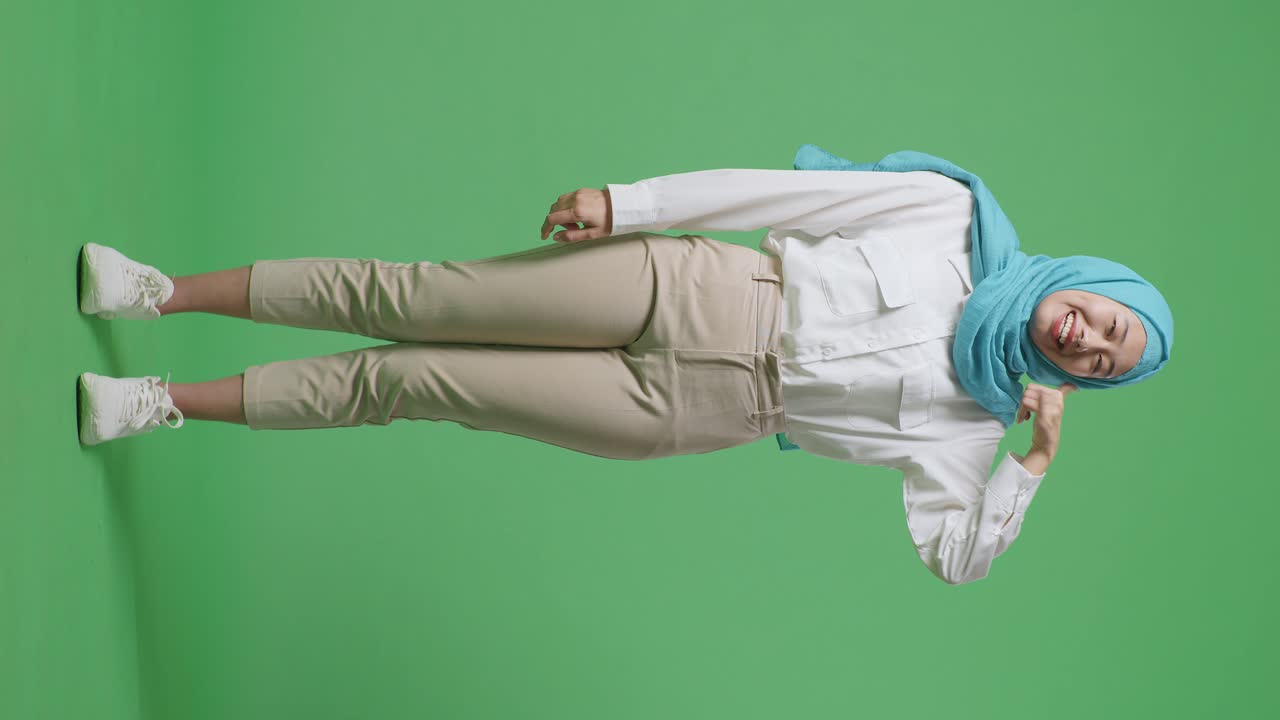 아시아 무슬림 여성이 미소 짓고 녹색 스크린 배경 스튜디오에 서있는 동안 나를 호출 제스처를합니다.