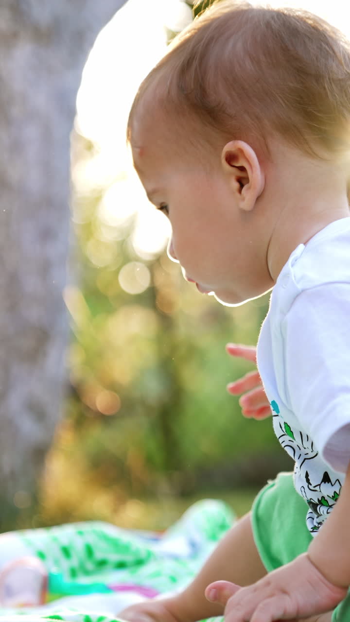 Nice little boy sitting on the blankets on the ground. Adorable child in the garden resting. Low angle view. Blurred backdrop. Vertical video