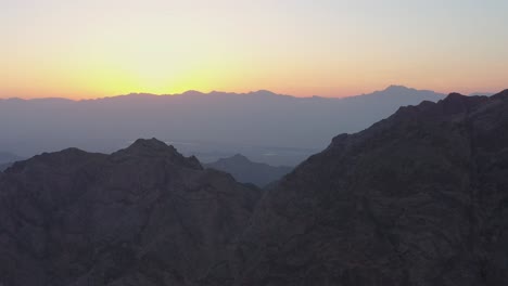 Retrocediendo-Desde-Un-Valle-En-La-Cresta-De-Una-Montaña-Mientras-El-Sol-Ardiente-Se-Pone-Detrás-De-Picos-Distantes