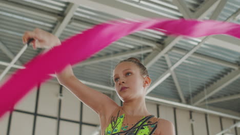 portrait of a young girl in leotard practising rhythmic gymnastics with a ribbon in a studio 1