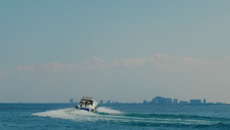 Speed-boat-with-American-flag-on-the-back-takes-sharp-turn-in-deep-blue-sea-with-city-behind-it