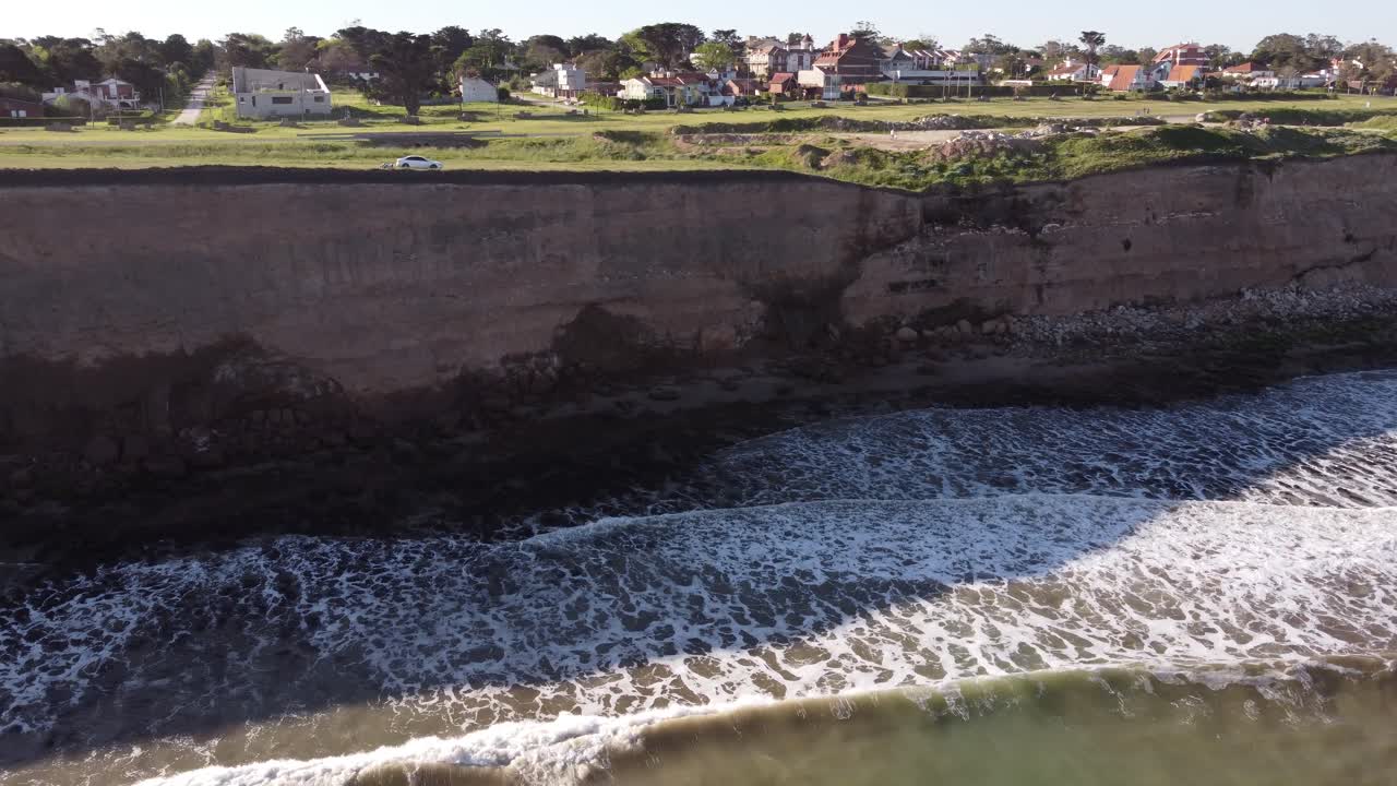 Aerial shot of giant cliffs and parking car on edge during sunny day - Waves of Ocean reaching cliff face - Mar del Plata,Argentina