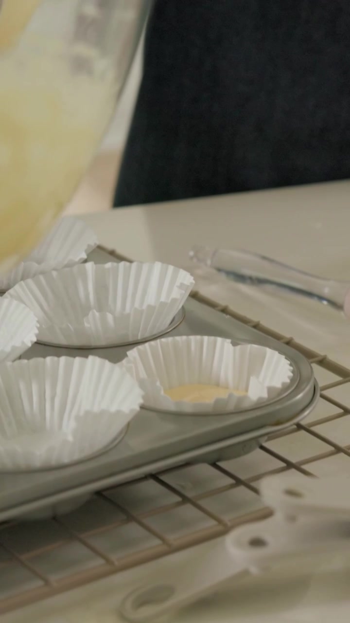 Video verticale: Mestolare l'impasto, adulto che guida un bambino con grembiuli a riempire uno stampo per muffin a casa con un mestolo.