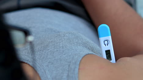 top view of man holds a digital thermometer underarm to measure the body temperature for fever