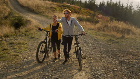 man and woman walking on path with bicycles. friends talking during walk