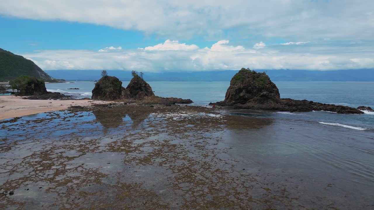 A mesmerizing drone shot captures a small island and a rocky mountain at the edge of the shore, with the vast ocean stretching out in the background.
