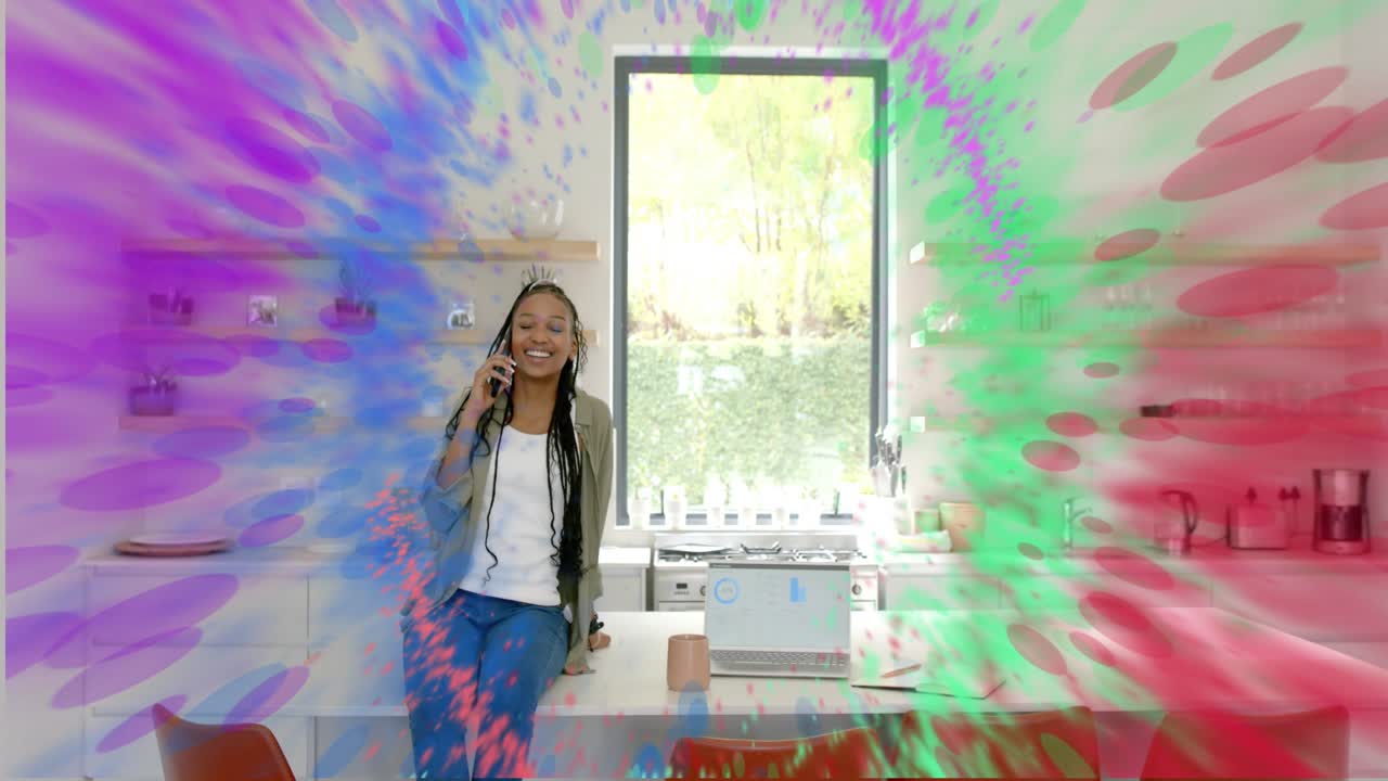 Woman leaning in kitchen speaking on phone, work call sparking expanding paint ring around laptop