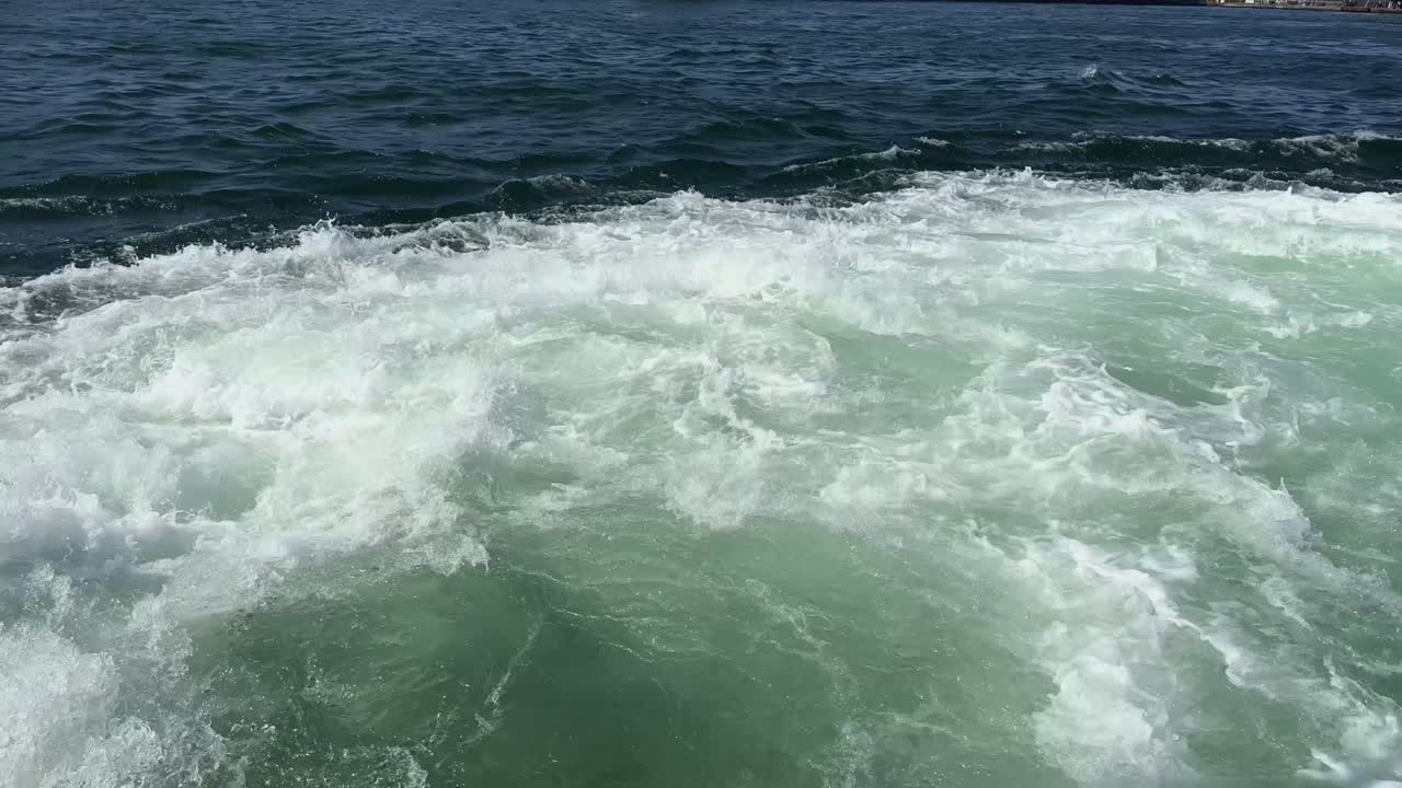 Overview of turquoise sea foam churning in swirling, powerful ocean current from boat motor