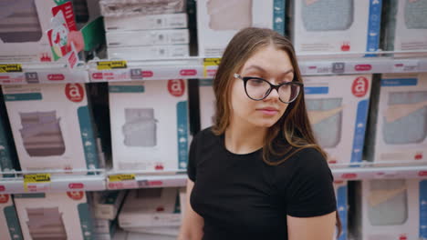 primer plano de una mujer joven caminando por un estante de la tienda lleno de productos de cama, mira a su alrededor, observando diseños de telas y opciones de textiles. decoración del hogar, ropa de cama y artículos esenciales para el dormitorio