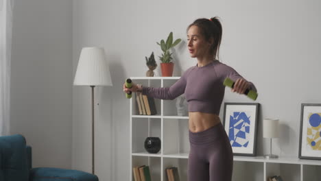 entraînement physique à domicile d'une jeune femme soulevant des haltères à deux mains portrait moyen dans le salon bien-être et mode de vie sain