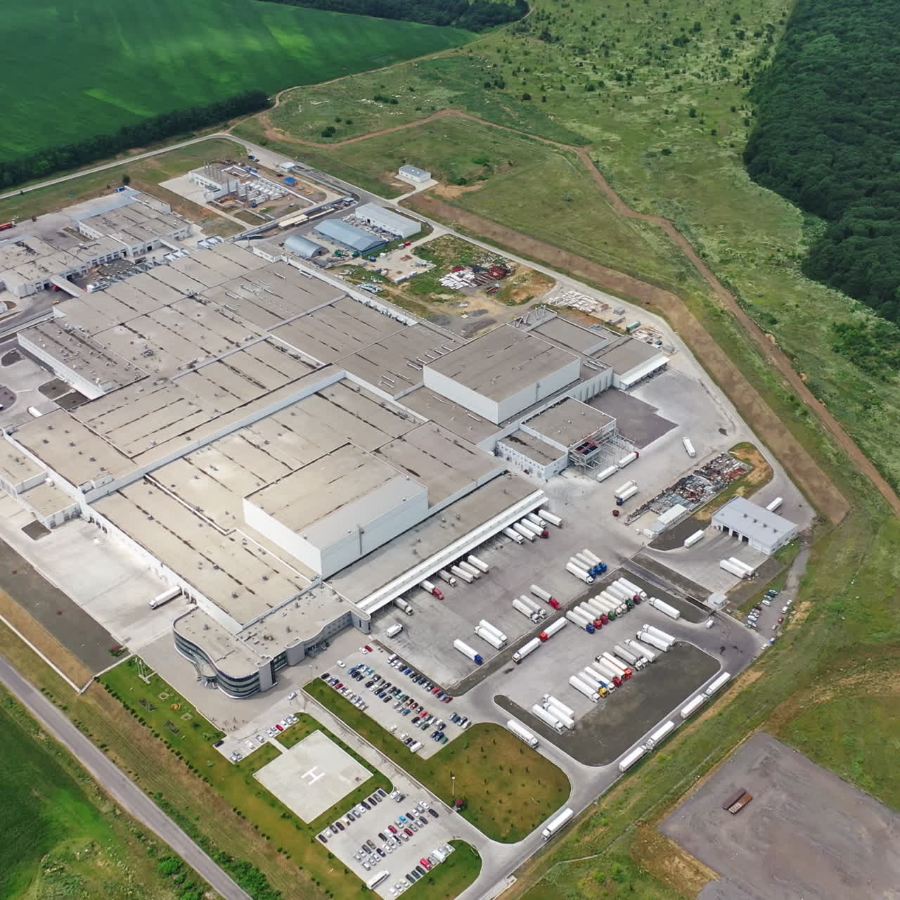 Big territory of industrial complex surrounded by green fields and forests. Top view on the large roofs of buildings of contemporary plant. Aerial view.