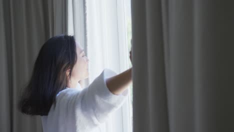 happy asian woman opening curtains in bedroom, in slow motion