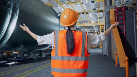 vista posterior de una ingeniera con casco de seguridad extendiendo los brazos mientras está de pie en una fábrica de fabricación de tubos