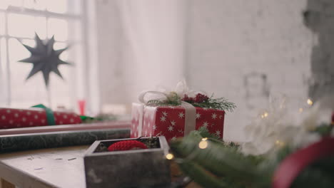 A-young-woman-decorating-a-gift-on-a-wooden-table-with-garlands-turns-over-and-puts-on-the-table-a-ready-made-Christmas-box-crushed-with-a-ribbon.