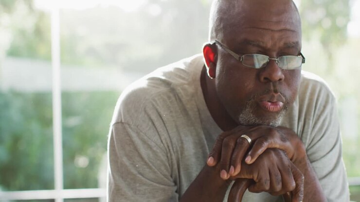 Portrait of thoughtful african american senior man sitting leaning on walking stick