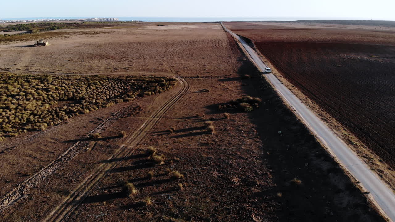 vuelo aéreo después de conducir un automóvil en una carretera rodeada de campos secos y luz solar