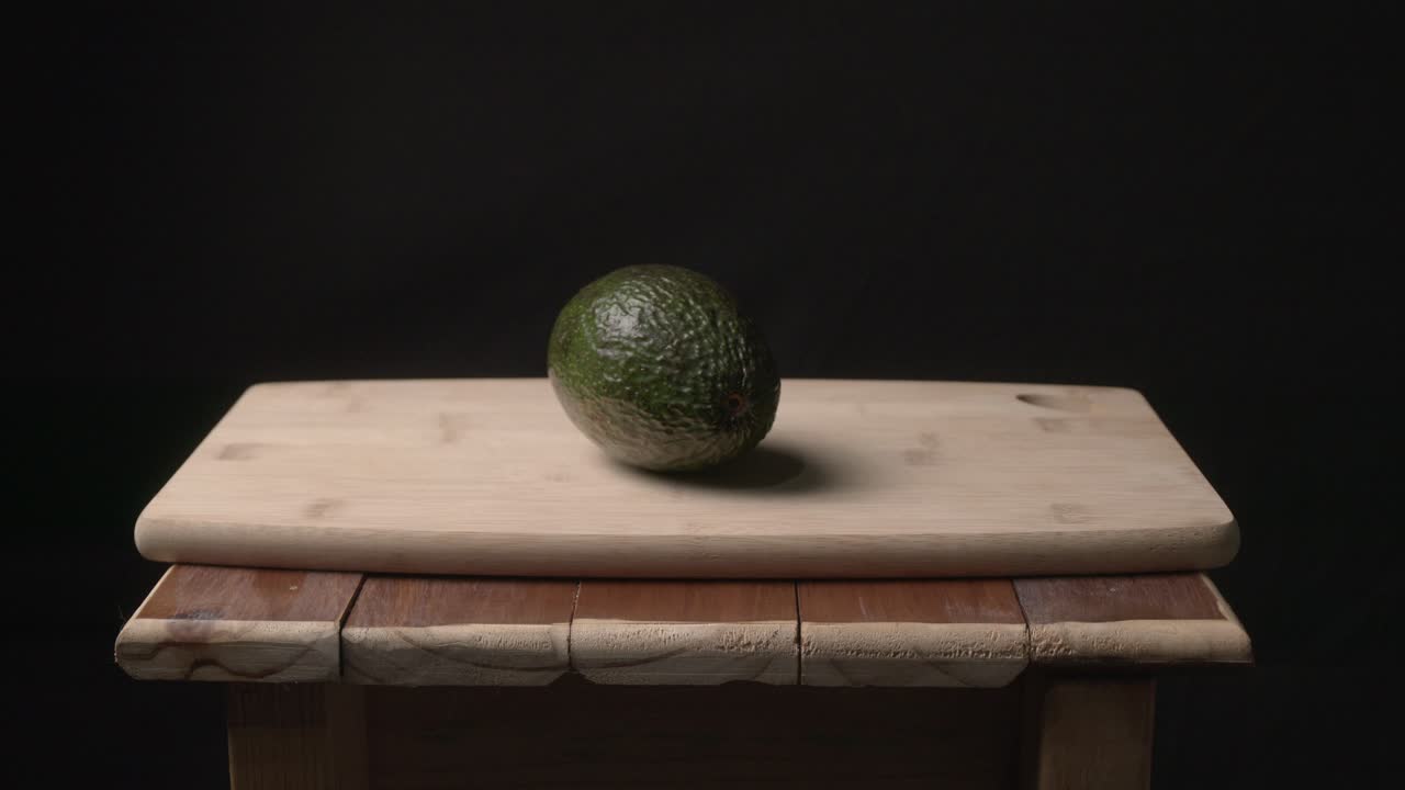 Un singolo avocado intero poggia su un tagliere di legno chiaro sopra un tavolo rustico, su uno sfondo scuro.