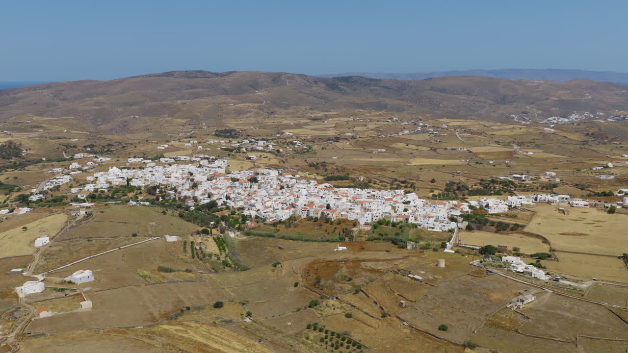 Rivelazione panoramica con drone di Kythnos Chora a mezzogiorno, che mostra case imbiancate a calce sotto il luminoso sole dell'Egeo.
