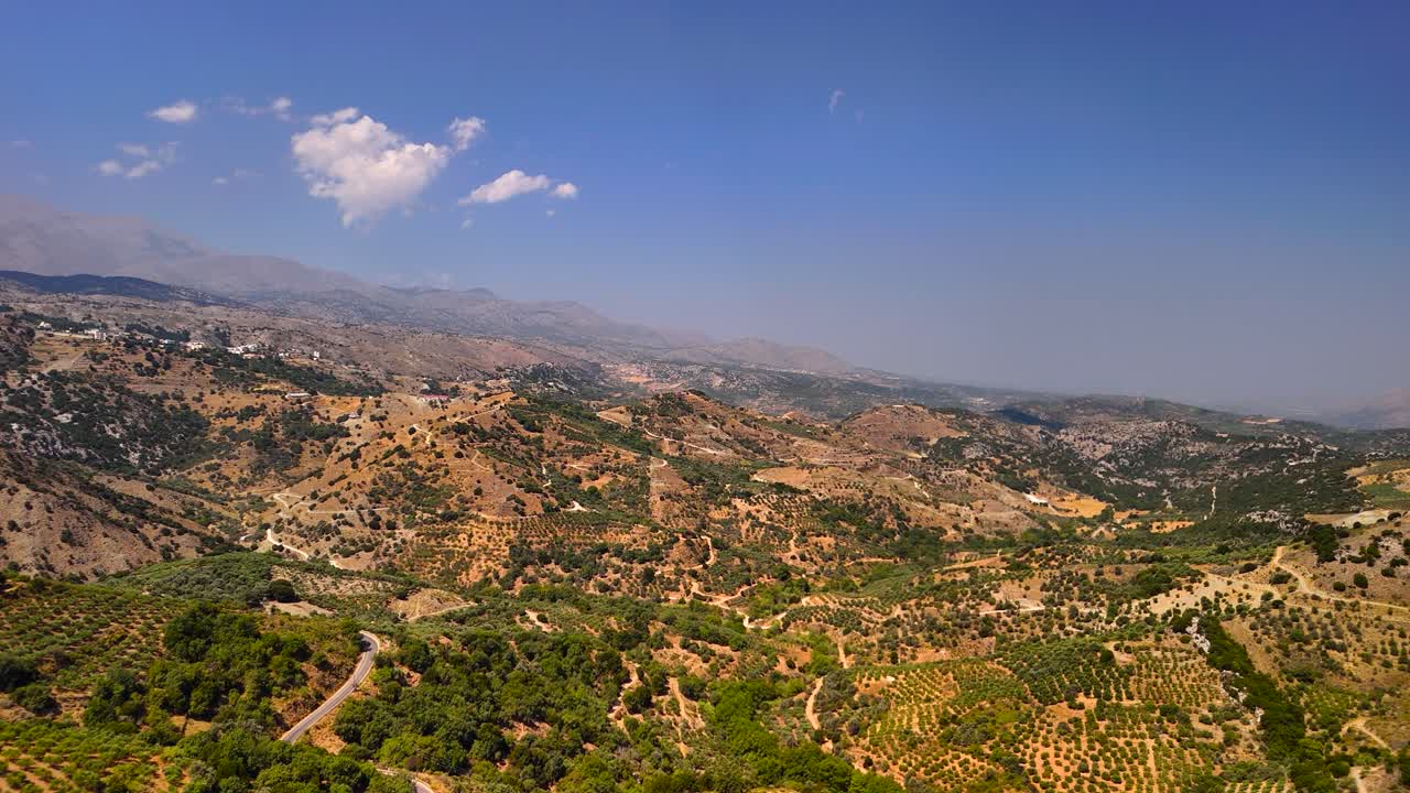 Wide view of lush green hills and sprawling valleys under a clear blue sky. The sun shines brightly over the countryside, creating a peaceful atmosphere