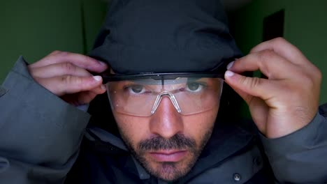 The-man,-with-a-serious-look-on-his-face,-dons-transparent-work-glasses-before-placing-a-hood-over-his-head,-preparing-for-an-intense-and-focused-task