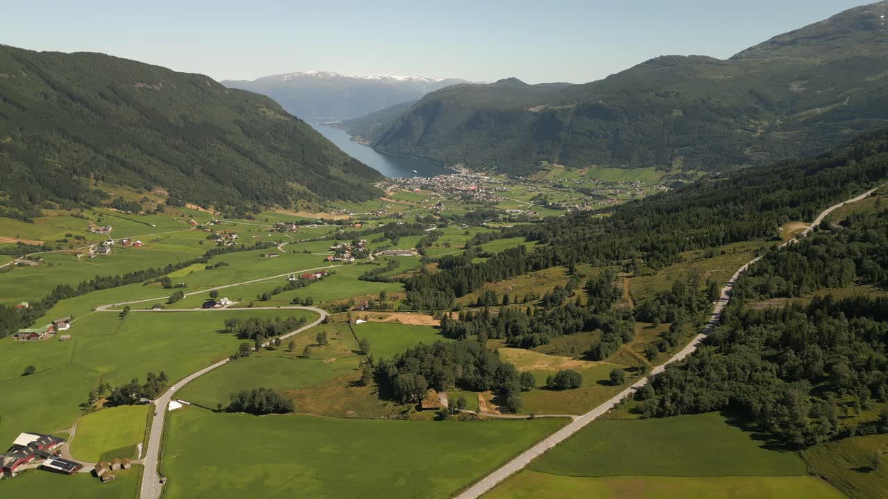 4K drone footage moving forward over Vik i Sogn, Vestland, Norway, showing green fields, winding roads, and the fjord leading toward the village centre on a clear summer day