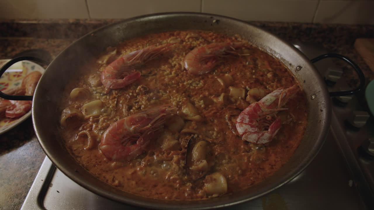 Paella di frutti di mare tradizionale valenciana che cuoce lentamente in una padella con gamberi, calamari, cozze, vapore e bolle