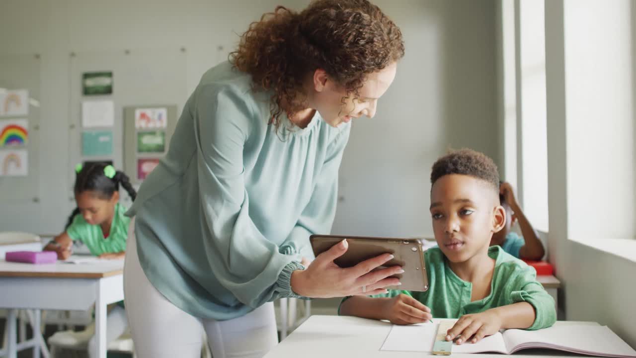 video de una feliz maestra caucásica explicando la lección en una tableta a un niño afroamericano