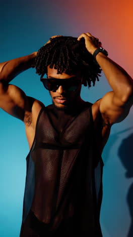 stylish man posing in mesh tank top and sunglasses with creative lighting