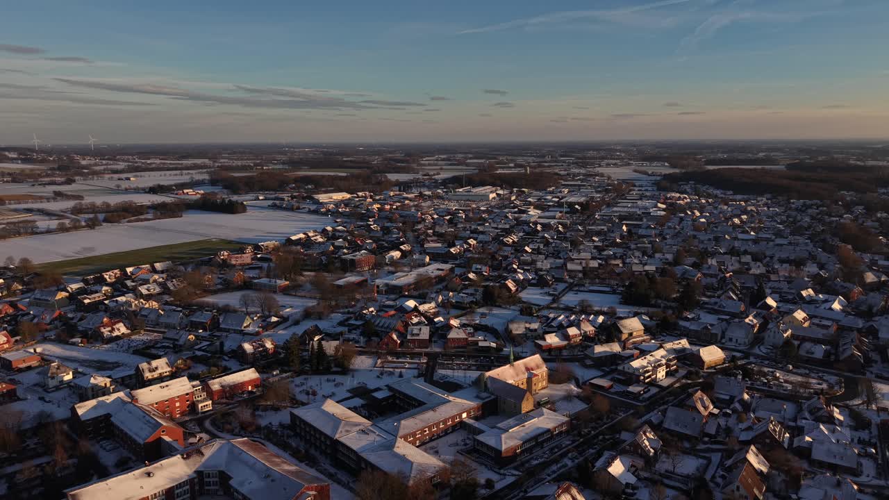 Frostklar vintermorgen i en tysk by med historiske bygninger og huse. Luftfoto, der stiger bredt. Gylden solopgang med landlige marker og vindmøller i det fjerne. Fredfyldt, sneklædt vinterdaggry