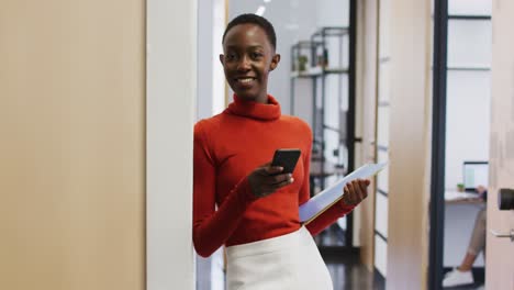 Portrait-of-african-american-woman-smiling-while-using-smartphone-at-office