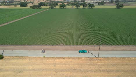 Drone-footage-of-light-blue-classic-mustant-driving-down-rural-country-roads-in-California,-during-the-day