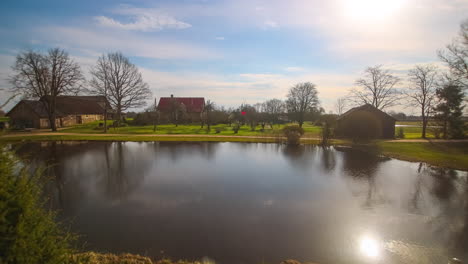 timelapse of a sunrise at a farm, sporadic clouds pass, as the sun rises it glistens off of a lake, the land and trees