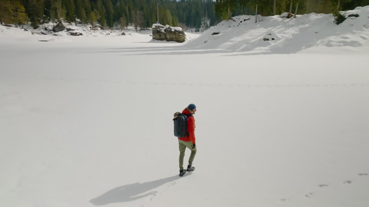 rastreando una foto aérea de un hombre con chaqueta naranja caminando por un lago cubierto de nieve congelada
