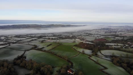 toma aérea sobre tierras de cultivo congeladas de devon en una mañana helada con niebla de río en el fondo