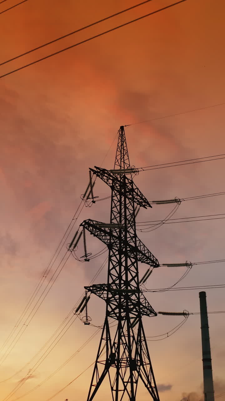 Electric towers near factory chimney with dark smoke. Transmission lines on background of harmful fumes from industry releasing from pipes at sunset. Environment pollution. Vertical video