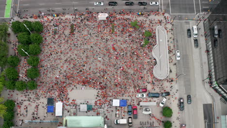 A-large-group-of-people-in-orange-shirts-gathers-in-downtown-Vancouver,-aerial-drone-slide-left