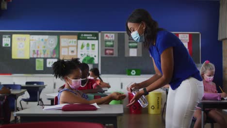 diversas maestras desinfectando las manos de las escolares durante la lección, todas con máscaras faciales