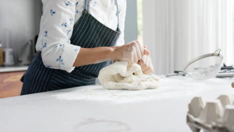 Happy-biracial-couple-wearing-aprons-and-making-dough-in-kitchen,-slow-motion