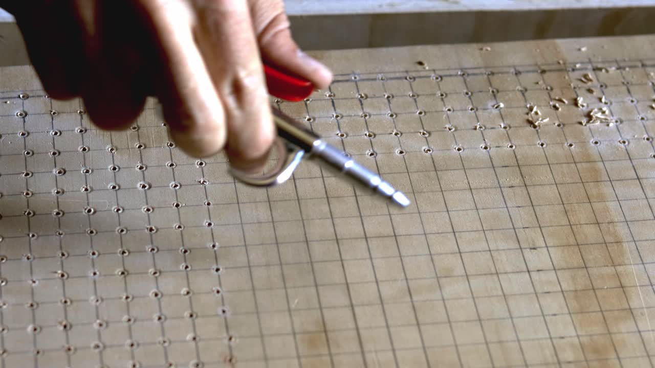 usando aire comprimido para soplar el polvo de sierra de una cuadrícula de agujeros perforados en madera contrachapada