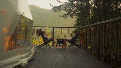 siblings watch movies on modern smartphones overlooking forest and mountains. adorable kids enjoy spectacular view on terrace surrounded by untouched nature