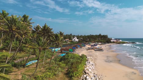 aerial-view-of-beautiful-Varkala-beach-with-coconut-trees-and-boats-on-the-sand-in-a-sunny-and-blue-sky-day---Kerala,-South-India