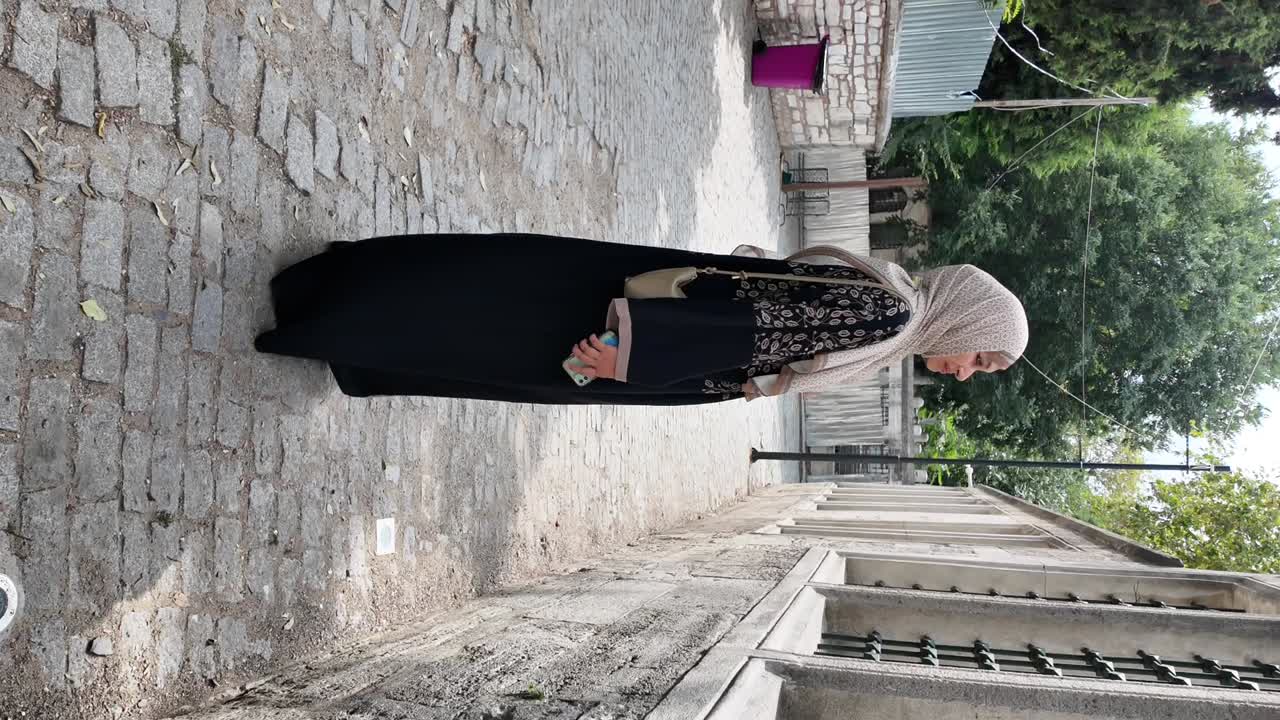Arnavut kaldırımlı bir sokakta başörtülü Müslüman bir kadın