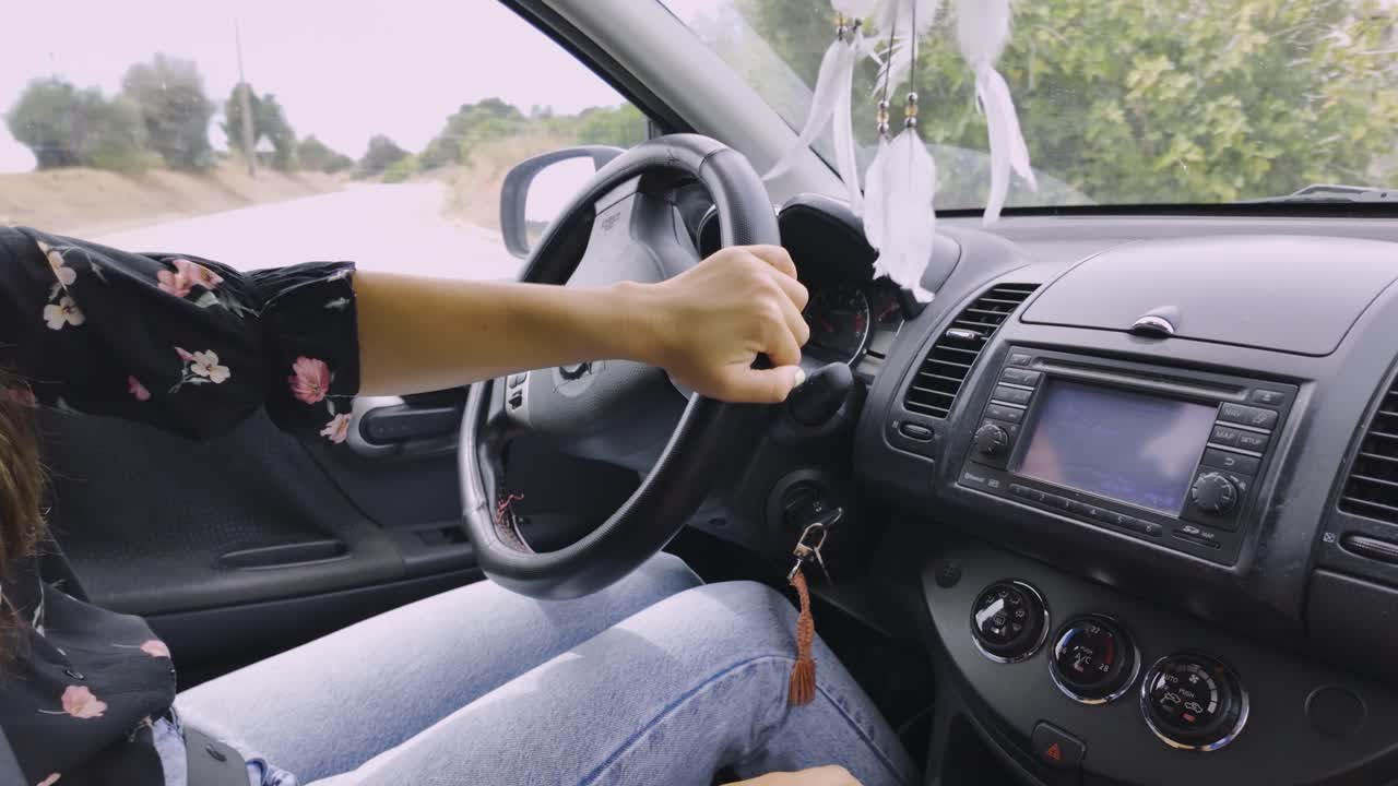 Close-up of a woman driving a car through an urban area, hands rotate wheel skillfully to make turn