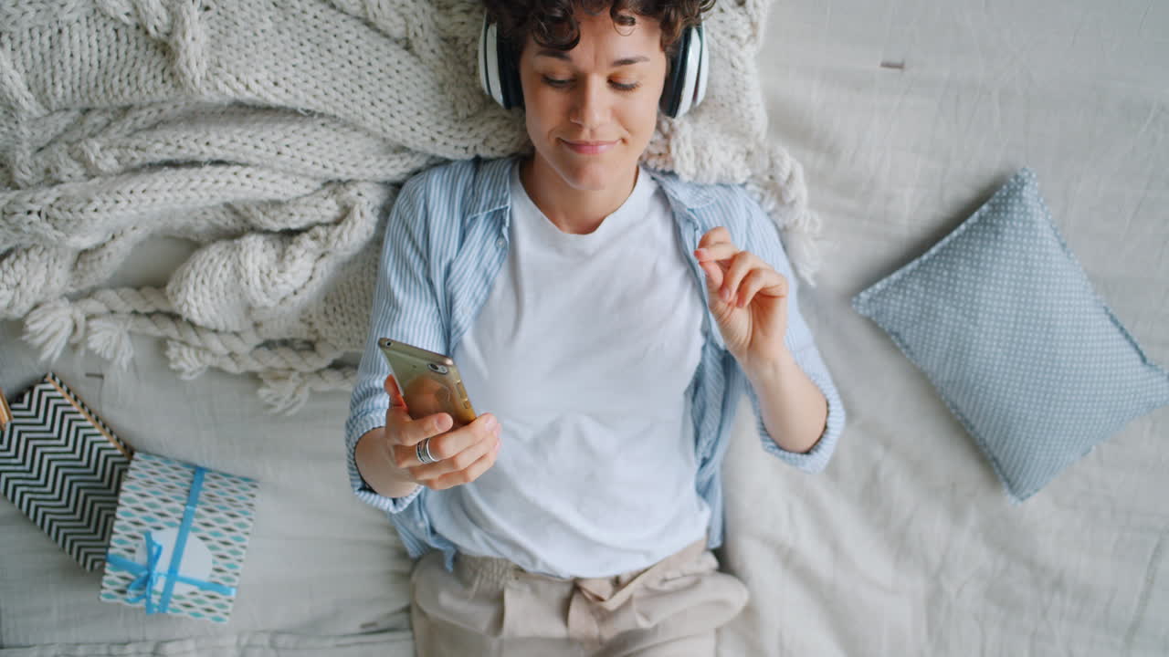 mujer relajándose en la cama con auriculares y teléfono