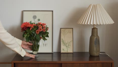 putting vase with orange flowers on wooden dresser by female hands