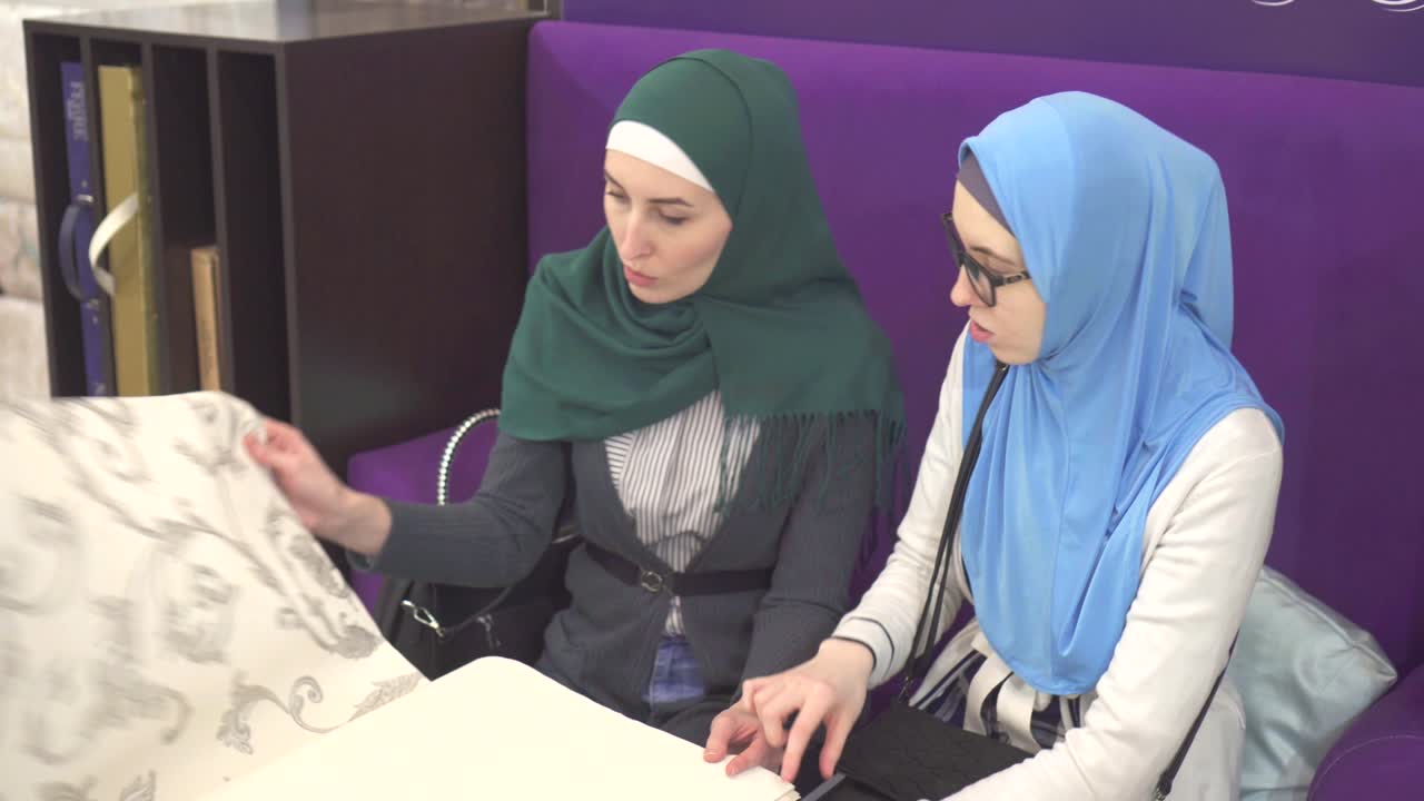 dos mujeres musulmanas jóvenes en hijab eligen papeles pintados del catálogo