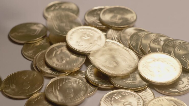 Versamento di monete indiane da 5 rupie placcate oro da un piccolo sacchetto di iuta su un tavolo, 4k, ripresa stabile.