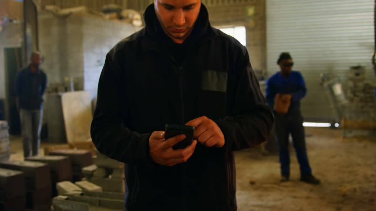 trabajador masculino que usa teléfono móvil en el taller 4k