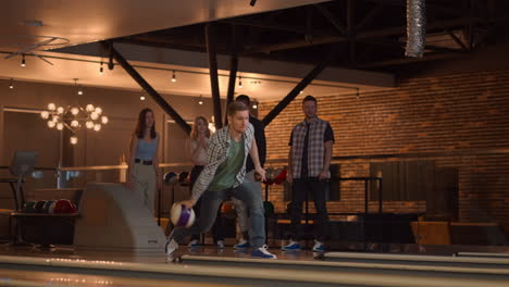 a caucasian man throws a bowling ball and knocks out a shot with one throw and hugs and rejoices with his friends. multi-ethnic group of friends bowling